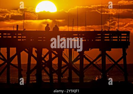 Isle Of Palms, Usa. Oktober 2024. Fisherman Silhouetten von einem dramatischen Sonnenaufgang werfen ihre Linien vor der Isle of Palms Pier am 11. Oktober 2024 in Isle of Palms, South Carolina. Hurrikan Milton zog 400 Meilen weiter nach Süden, führte aber herbstliches Wetter entlang der Küste, während die Stürme aufwachen. Quelle: Richard Ellis/Richard Ellis/Alamy Live News Stockfoto