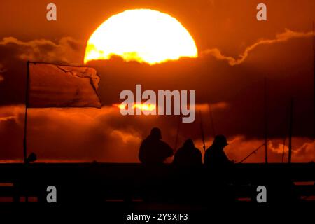 Isle Of Palms, Usa. Oktober 2024. Fisherman Silhouetten von einem dramatischen Sonnenaufgang werfen ihre Linien vor der Isle of Palms Pier am 11. Oktober 2024 in Isle of Palms, South Carolina. Hurrikan Milton zog 400 Meilen weiter nach Süden, führte aber herbstliches Wetter entlang der Küste, während die Stürme aufwachen. Quelle: Richard Ellis/Richard Ellis/Alamy Live News Stockfoto