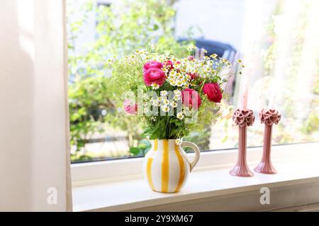 Wunderschöne Ranunkelblumen und Kamillen in Vase auf Fensterbank drinnen Stockfoto