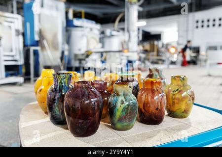 Viele farbenfrohe Glasvasen in der Glasbläserei Fabrik mit Ofenausrüstung auf Hintergrund gesetzt. Handgefertigtes, handgefertigtes Blasglas Stockfoto