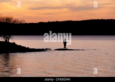 Silhouette eines Fischers, der während des Sonnenuntergangs im Wasser steht Stockfoto