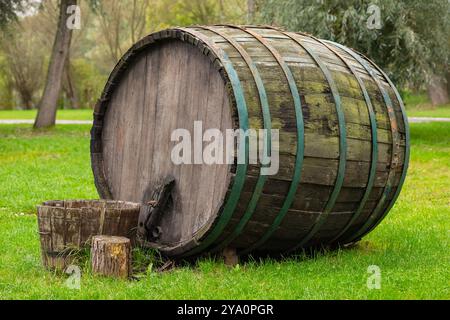 Großes Vintage-Holzweinfass mit grünen Metallbändern auf grünem Gras in einem Park an einem sonnigen Tag. Konzept der traditionellen Weinherstellung, rustikale Deko Stockfoto