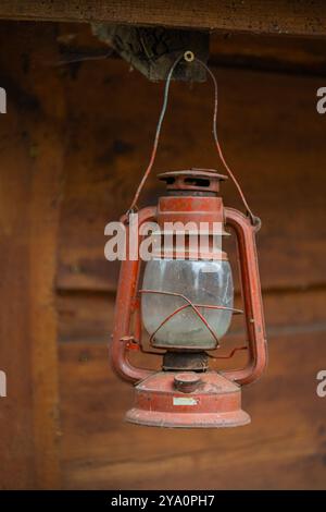 Vintage rote Kerosin-Laterne, die an einem Holzbalken hängt und rustikalen Charme und Nostalgie zeigt. Konzept mit Retro-Beleuchtung, antikem Dekor und Outdoor-Ausrüstung Stockfoto