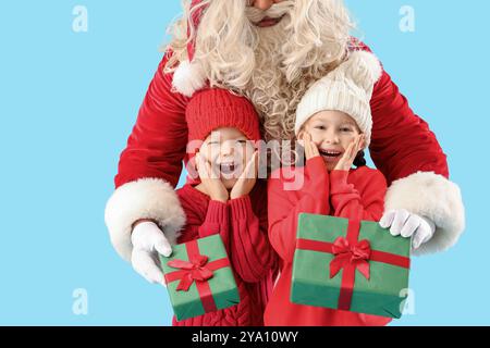 Überraschte kleine Kinder, die Weihnachtsgeschenke vom Weihnachtsmann auf blauem Hintergrund erhalten Stockfoto