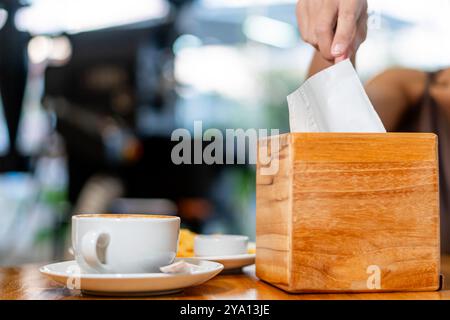 Eine Person, die ein Stück Papier in eine hölzerne Wahlurne auf einen Tisch wirft. Im Vordergrund gibt es eine Tasse Kaffee und einen kleinen Teller mit Snacks. Die Stockfoto