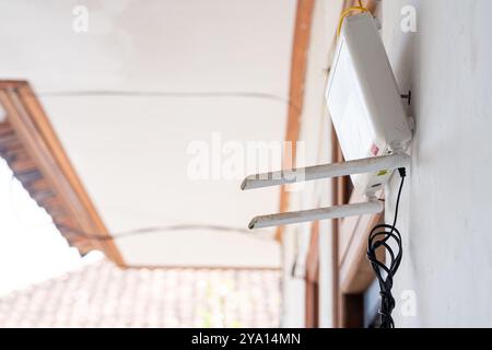 Nahaufnahme eines drahtlosen Routers, der an einer Wand montiert ist und zwei Antennen aufweist. Der Router ist mit Kabeln verbunden, und der Hintergrund ist verschwommen Stockfoto