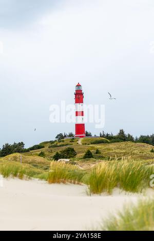 Der Leuchtturm ist in kräftigen roten und weißen Streifen gestrichen und blickt auf Sanddünen und eine grasbewachsene Landschaft, umgeben von einem bewölkten Himmel mit Vögeln, die ab fliegen Stockfoto