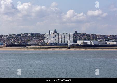 Blick auf die Küste mit einem Streifen Strand und urbanem Hintergrund mit markantem Turm in klarem Himmel, Liverpool Stockfoto