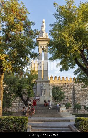 Denkmal mit Statuen umgeben von Bäumen und Menschen in der Abenddämmerung, Sevilla Stockfoto