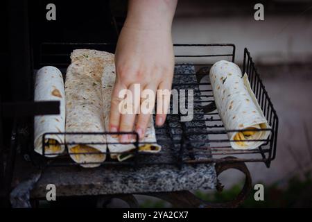 Kochen unter freiem Himmel. Eine Frau kocht Pita Tortillas auf einem Grillfeuer im Freien. Vegetarische Grillgerichte. Handgerollte Gemüsepackungen. Stockfoto