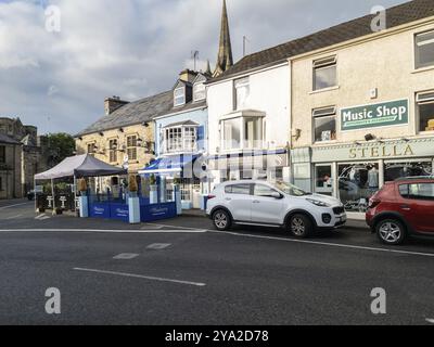 Kleine Läden entlang einer Straße mit geparkten Autos und einer Kirche, Donegal Stockfoto