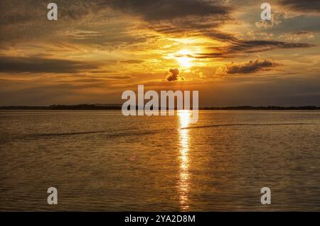 Ein leuchtend orangener Sonnenuntergang spiegelt sich auf der Wasseroberfläche, Uebersee, Chiemsee Stockfoto