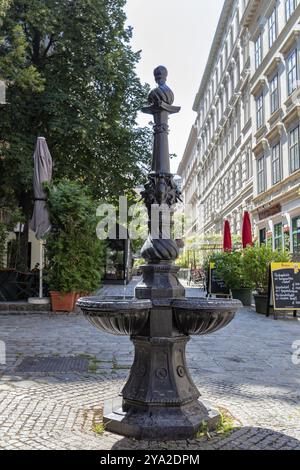 Dekorativer Brunnen mit Büste in einem sonnigen Innenhof umgeben von alten Gebäuden und Grün, Wien Stockfoto