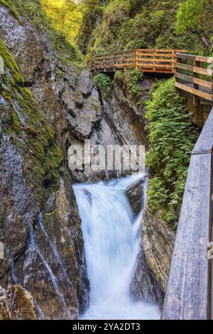 Ein schmaler Wasserfall verläuft durch eine felsige Schlucht mit einem Plankenweg in der Nähe, der den Geist des Abenteuers weckt, die Wimbachklamm-Schlucht Stockfoto