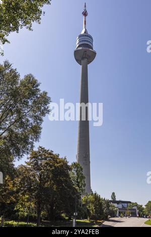 Ein hoher Fernsehturm erhebt sich in den blauen Himmel über grünen Bäumen, Wien Stockfoto