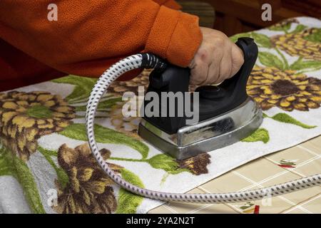 Nahaufnahme der Hände der Frau, die bügelt. Hände einer Seniorin, die ein Handtuch bügelt Stockfoto