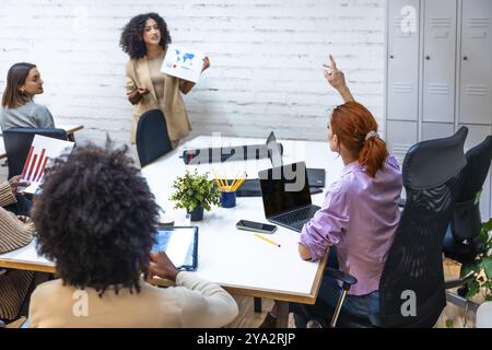 Frau, die Fragen während einer Datenpräsentation einer Kollegin in in einem Coworking stellt Stockfoto