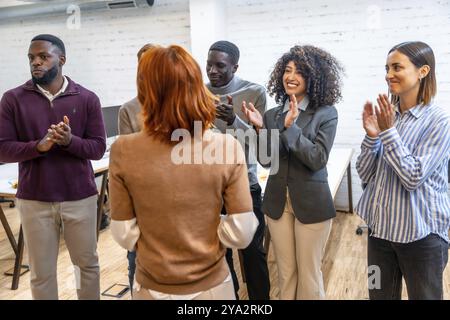 Gruppe verschiedener Kollegen, die einer Frau bei der Projektpräsentation im Coworking applaudieren Stockfoto
