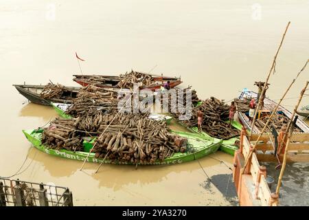 Mit Brennholz beladene Boote für Einäscherungszeremonien auf dem Fluss Ganges, Marnikarnika Ghat, Varanasi, Uttar Pradesh, Indien. Stockfoto