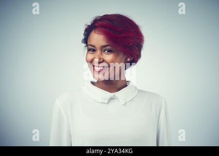 Afrikanische Frau, glücklich und Haarpflege im Studio für Selbstvertrauen, Textur und Kosmetik mit roter Färbung. Weibliche Person, Porträt und positive Stimmung auf Grau Stockfoto
