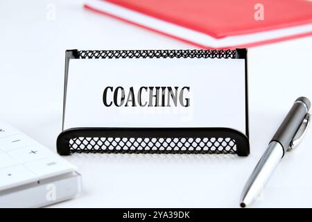 Geschäftskonzept. Der Satz, Text, Wortwahl COACHING ist auf einer weißen Visitenkarte in einem Stand auf einer weißen Oberfläche geschrieben. Stockfoto