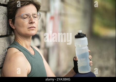 36 Jahre alte weiße Frau, die eine Flasche Wasser trinkt, sich nach dem Training entspannt, Brüssel, Belgien, Europa Stockfoto