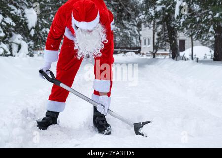 Der Weihnachtsmann reinigt im Winter draußen nach einem Schneefall Schnee mit Schaufel. Die Straßen im Dorf zu reinigen, die Passage für Autos freizumachen, schwierig Stockfoto