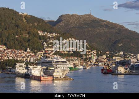 Stadt und Hafen von Bergen in Norwegen mit den Bergen Floyen und Ulriken. Im Hafen ein Kreuzfahrtschiff und Offshore-Versorgungsschiffe. Stadt und Harbou Stockfoto