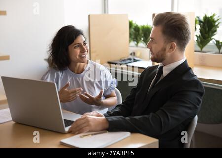 Ein positives Paar von indischen und kaukasischen Bürokollegen, die über die Arbeit diskutieren Stockfoto