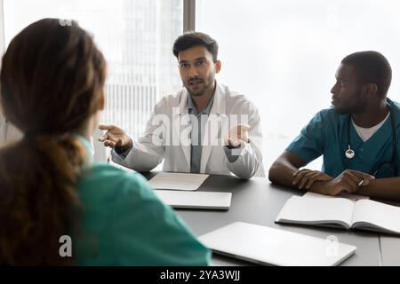 Junger männlicher Arzt spricht über multikulturelles Team-Treffen in der Klinik Stockfoto
