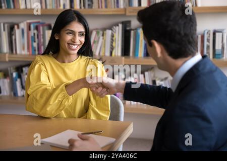 Glückliche indische Studentin, die mit dem Lehrer in der Bibliothek die Hand schüttelt Stockfoto