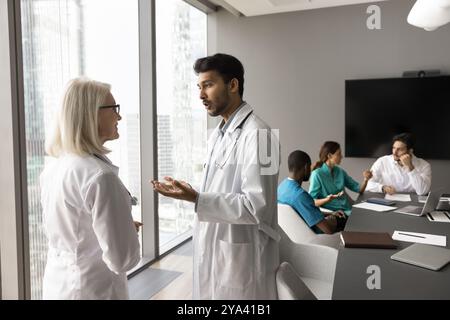 Junger männlicher Arzt spricht mit älteren Kolleginnen in der Vorstandssitzung Stockfoto