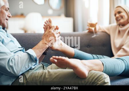 Zu Hause, reif und zu zweit mit Fußmassage und Pflege zusammen auf Sofa mit Liebe und Lächeln. Wein, Getränke und Füße unterstützen Sie mit Wellness und Verbundenheit Stockfoto