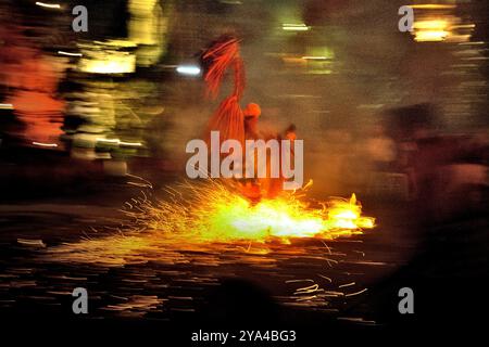 Ein Feuertanz-Darsteller läuft während der Kecak- und Feuertanz-Show in Ubud, Gianyar, Bali, Indonesien über einen Haufen brennender Kokosnüsse. Stockfoto