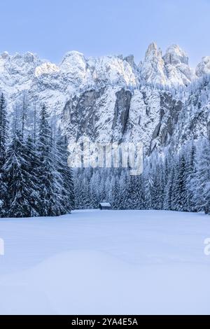 Eine märchenhafte Winterlandschaft in den italienischen Alpen, mit schneebedeckten Feldern und einer kleinen Hütte inmitten der Bäume. Die majestätischen Dolomitengipfel erheben sich Stockfoto