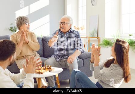 Lächeln und Lachen im Wohnzimmer Familie alte Eltern Tochter Sohn genießt Schach während des Familienurlaubs. Familienmomente älterer Ehepaare Stockfoto