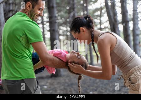 Glückliche Eltern spielen mit ihrer lächelnden Tochter in einem sonnendurchfluteten Wald. Die Familie genießt eine unterhaltsame Outdoor-Aktivität, die die Freude der Naturforscher zeigt Stockfoto