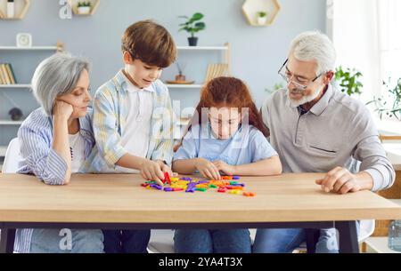 Großeltern unterrichten ihren Enkeln Alphabet mit Briefen, die zu Hause am Tisch sitzen. Stockfoto