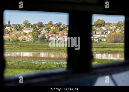 Ein Blick durch das Fenster eines Vogelhäuschens im RSPB Pulborough Brooks Naturschutzgebiet in West Sussex in England, mit Häusern im Hintergrund. Stockfoto