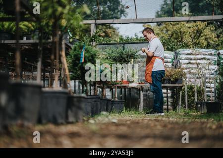 Junger Gärtner mit Down-Syndrom, der Pflanzen im Gewächshaus pflegt Stockfoto