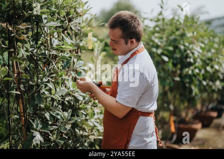 Junger Gärtner mit Down-Syndrom, der sich um Pflanzen im Garten kümmert Stockfoto