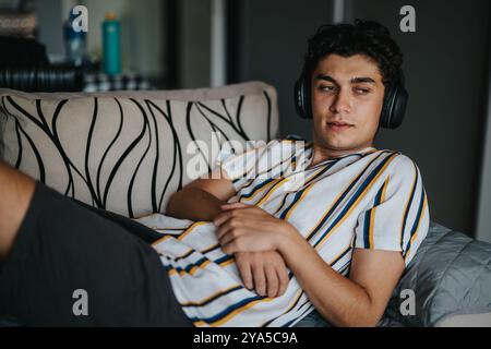 Junger Mann, der sich auf dem Sofa mit anliegenden Kopfhörern entspannt Stockfoto