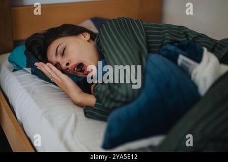 Frau gähnt im Bett unter gemütlichem gestreiftem Bettzeug Stockfoto