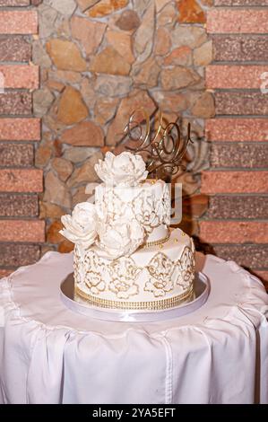 Elegante dreistufige Hochzeitstorte mit Gold- und Blumenakzenten. Stockfoto