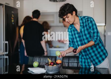 Junger Mann, der Obst in der modernen Küche mit Freunden zubereitet Stockfoto