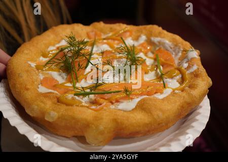 Nahaufnahme eines langos, typisch ungarische Spezialitäten, mit Sauerrahm und Fischlachs auf einem weißen Gericht auf einem braunen Tisch, frittiertem Teig bei A christ Stockfoto