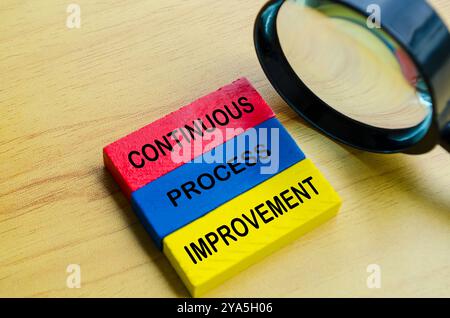 Text zur kontinuierlichen Prozessverbesserung auf mehrfarbigen Holzblöcken mit Lupenhintergrund. Konzept der kontinuierlichen Verbesserung. Stockfoto