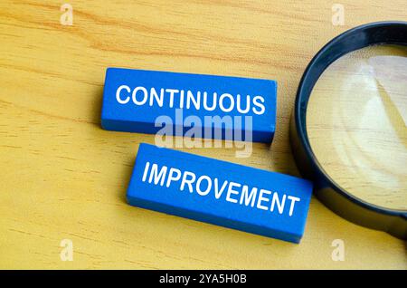 Kontinuierlicher Verbesserungstext auf blauen Holzblöcken mit Lupenhintergrund. Konzept der kontinuierlichen Verbesserung. Stockfoto