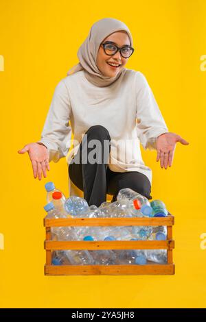 Hijab-Frau zeigt Plastikflasche in Holzlager isoliert Stockfoto