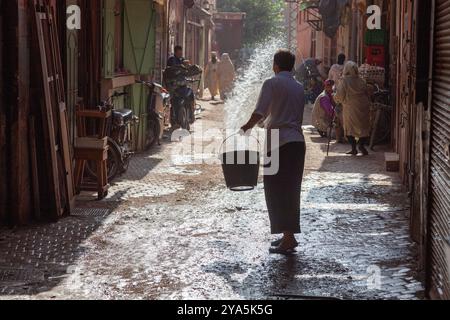 Die Morgensonne taucht diese Straße in der Medina von Marrakesch, wo die ersten Arbeiter beschäftigt sind Stockfoto